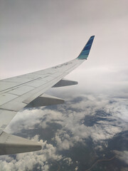 Obraz premium Airplane wing gliding above blue ocean and soft white clouds during flight, showcasing the serene view from the window and the calm contrast between sky, sea, and the aircraft structure.