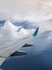 Fototapeta premium Airplane wing gliding above blue ocean and soft white clouds during flight, showcasing the serene view from the window and the calm contrast between sky, sea, and the aircraft structure.