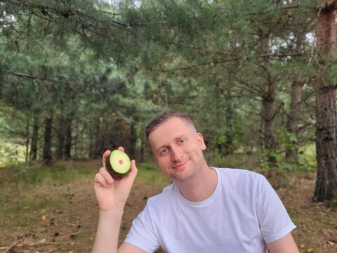 Smiling man holding a sliced avocado against a natural background