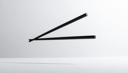 Two black chopsticks are suspended in the air against a clean white background, casting a soft shadow below.
