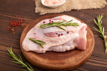 Raw Turkey Thigh with spices on cutting board on brown wooden, linen textile. side view, close up