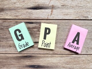 Grade Point Average or GPA acronym word written on multicolour paper against wood surface. 