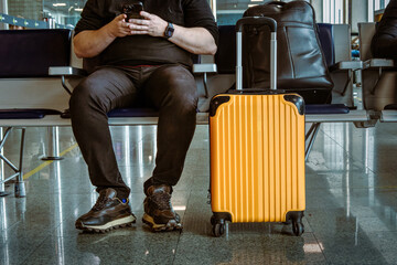Anonymous man with a yellow suitcase waiting at the airport