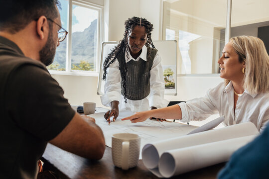 Architects discussing designs at office table with plan drawings and teamwork dynamics.