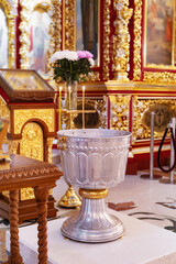 Baptismal font in ornate Christian church interior with candles and icons. Religious symbol of faith, christening tradition, and Orthodox baptism ceremony.
