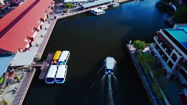 Wide drone perspective of ferry navigating Melaka River with the historic city visible.