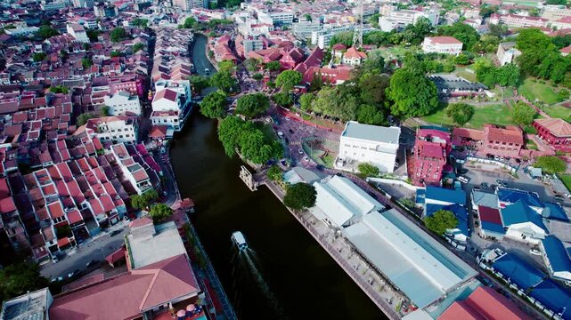 Drone orbit shot capturing Red Square heritage buildings with riverboat on Melaka River.