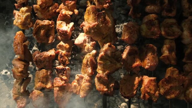 Top view of many juicy meat skewers grilling over hot charcoal, brightly lit by sunlight. Skewers are rotated by grill master for even cooking. appetizing barbecue in progress over glowing coals.
