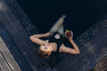 Young woman relaxing in swimming pool with cocktail enjoying summer vacation