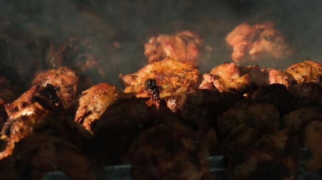 Juicy, steaming meat skewers grilling over hot charcoal. One skewer with shiny meat is removed and placed back by grill master. Cooking meat outdoors and eating with strong appetite in natural setting