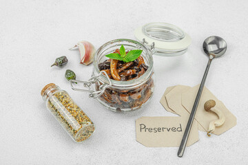 Preserved shimeji mushrooms in a glass jar with herbs and spices on a light background