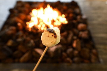 A roasted marshmallow over a campfire with warm flames, evoking camping, fire-lit nights, and enjoying sweets outdoors.
