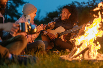 Man playing the guitar next to the campfire