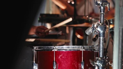 Musician's hands drumming red snare with wooden sticks, generating dynamic rhythm during energetic christian worship performance, surrounded by stage musical instruments