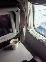 Coffee cup on an airplane tray beside the window, with a clear view of the aircraft wing under bright daylight during flight.