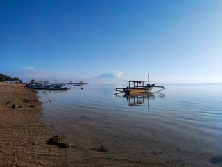 Morning serenity at Sanur Beach with fishing boats resting on calm waters and Mount Agung rising in the clear horizon under the bright tropical sky.