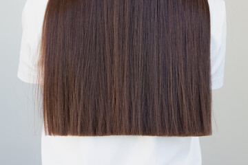 Brunette woman in white tshirt with beautiful long, straight hair stands with her back to the...