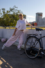 Obraz premium A young woman in a white T-shirt and pink sweatpants is doing physical exercises next to a bicycle