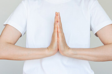 Woman in white t-shirt with hands in namaste gesture close-up, palms pressed together gently, fingers pointing upward