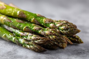 Close up of grilled asparagus seasoned with olive oil, salt and pepper lying on gray marble surface