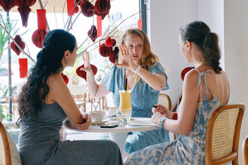 Young businesswomen sitting at table in cafe. Girl tells her colleagues information. Teamwork, business meeting. Freelance work.
