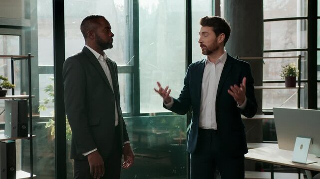 Two serious multiracial business men team businessmen talking in office company meeting multiethnic colleagues partners discuss work job deal Caucasian African American employers talk negotiation