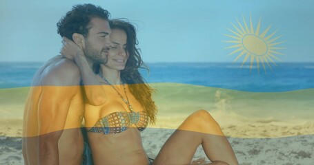 Fototapeta premium Embracing couple wearing swim trunks and bikini top sitting on calm beach, with flag overlay