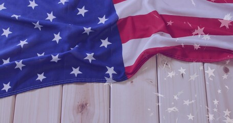 Displaying draped American flag on light wood planks, with star reflections across surface