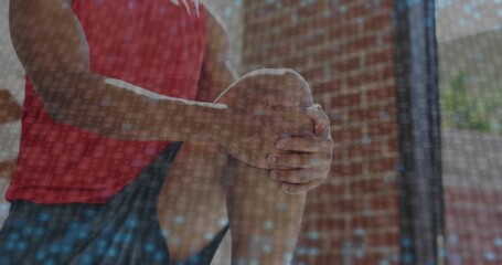 Stretching athlete pulling knee toward chest in gym with brick wall, wearing red top and shorts