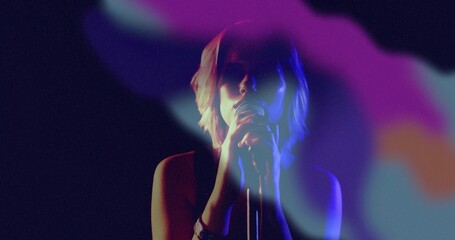Singing teenage singer wearing sleeveless top holding microphone center stage, with colored haze