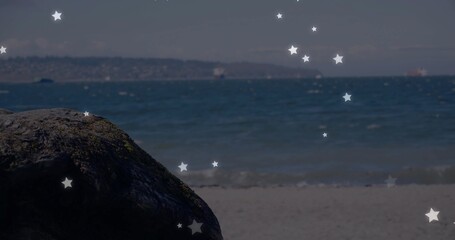 Fototapeta premium Moss-covered rock resting on sandy beach, with gentle waves and star-shaped overlays, copy space