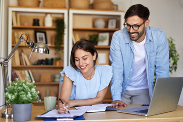 Fototapeta premium Two people engage in a productive session in a home office. One person writes notes while the other observes, creating a lively and collaborative atmosphere.