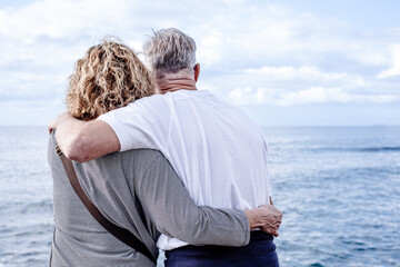 Rear view of mature romantic embracing  couple face the sea looking at horizon over water, two carefree people stay together expressing love and tenderness enjoying nature and vacation