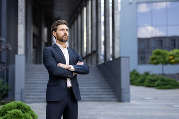 Portrait of a successful businessman standing with crossed arms in front of a modern office...