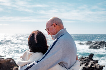 Fototapeta premium Smiling caucasian senior couple tenderly embraced enjoying a sunny day at sea. Healthy lifestyle, vacation or retirement