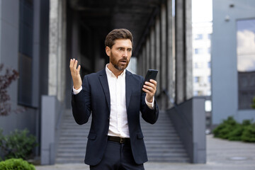 Stressed businessman raising his hand in despair while reading disappointing news on his...