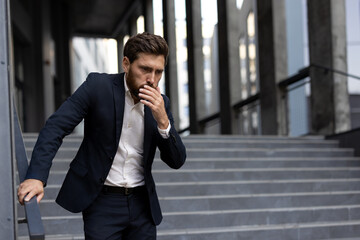 Businessman suffering from nausea covering his mouth with hand while standing on stairs and feeling...
