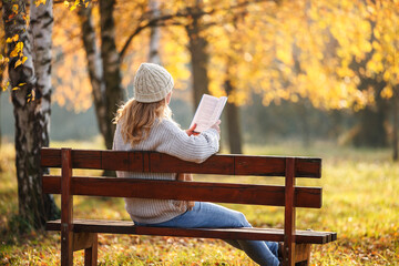 Woman sitting on bench reading book in autumn park enjoying mindfulness and calm moment for herself