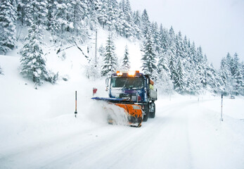 A snow plow vehicle is driving down a winter snowcovered road