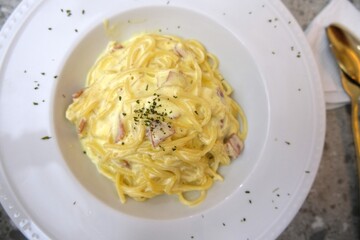 Delicious creamy spaghetti carbonara pasta topped with herbs and served on a white plate, representing Italian cuisine and comfort food.  
