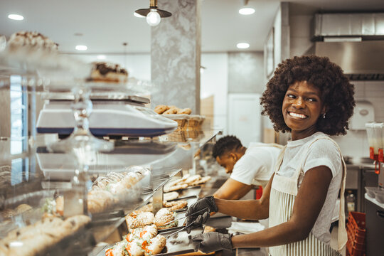 Smiling Bakery Employee Working Behind Display Counter in Cozy Pastry Shop