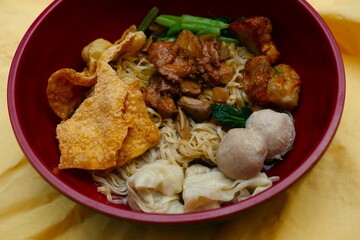Bowl of Indonesian bakmi noodles served with dumplings, meatballs, fried wonton, vegetables, and seasoned chicken pieces on top.  
