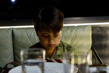 Modern childhood: a young boy with a smartphone at a dinner.