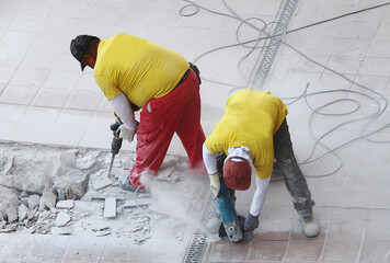Dos obreros trabajando en equipo con máquina martillo taladradora hidráulico, radial y cables en obra de reforma de suelo de patio