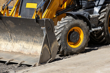 A close-up view of the rugged front loader bucket and large tire of a heavy construction vehicle, ready for work on a dirt and gravel site. The powerful machinery highlights industrial strength.