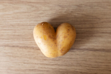 A heart-shaped potato sits on a wooden surface, displaying its unusual shape. This interesting vegetable can spark creativity in cooking or simply serves as a quirky decoration