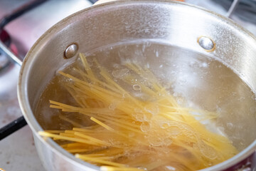 Cooking spaghetti in a stainless steel pot filled with boiling water, showcasing the pasta's texture and bubbles, creating a vibrant culinary scene in a kitchen environment