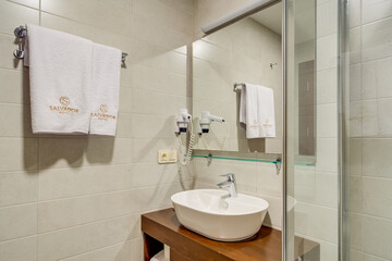 A spacious modern bathroom with a clean design, featuring a glass shower, a wooden vanity unit, and tiled walls. The elegant fixture placement creates a comfortable and functional space.