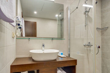 A spacious modern bathroom with a clean design, featuring a glass shower, a wooden vanity unit, and tiled walls. The elegant fixture placement creates a comfortable and functional space.