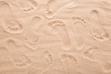Background of people footprints on dry light brown sea sand. Closeup. Top down view.